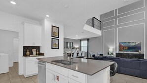 Una cocina moderna con armarios blancos, una isla central y una zona de comedor con un sofá gris.