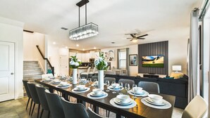A dining area with a long table set for six, a modern chandelier, and a ceiling fan. - Last Minute Disney! Private Pool, Hot Tub, Game Room & Themed Bedrooms. Book Now! #87159 (Orlando)