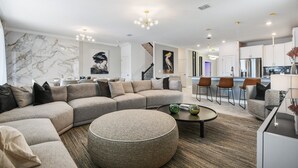 Ein modernes Wohnzimmer mit Ecksofa, rundem Hocker und einem Essbereich mit Barhocker.