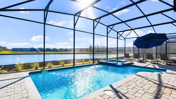 Ein Pool mit Blick auf einen See und Gebäude in der Ferne, umgeben von einer überdachten Liegefläche mit Liegestühlen und Sonnenschirm.
