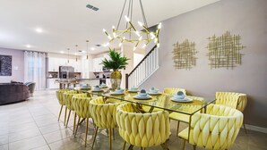 Un comedor con mesa de vidrio, sillas tapizadas en amarillo y una lámpara moderna.