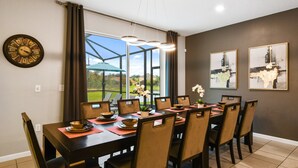 A dining area with a long table, chairs, a clock, and artwork on the walls.