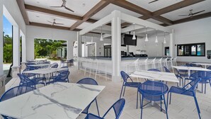 A spacious outdoor dining area with white tables and blue chairs, a bar area with a flat-screen TV, and ceiling fans. - Last Minute Disney! Private Pool, Hot Tub & Themed Bedrooms. Book Now! #89755 (Orlando)
