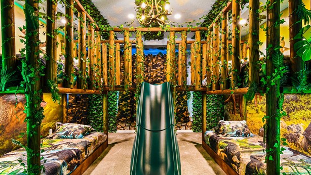 A room with a central slide, wooden pillars with vines, and dinosaur-themed bedding.