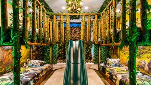 A room with a central slide, wooden pillars with vines, and dinosaur-themed bedding.