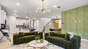 A modern living room with green sofas, a marble coffee table, and a kitchen in the background.