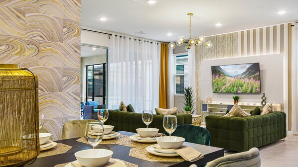 A modern living room with a dining area, featuring a sofa set, a TV mounted on the wall, and a decorative vase.