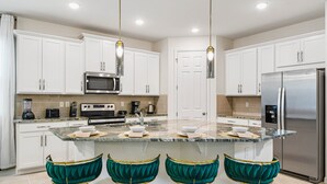 A modern kitchen with white cabinets, stainless steel appliances, a granite countertop, and teal upholstered chairs.