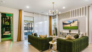 A modern living room with green sofas, a round coffee table, and a flat-screen TV on the wall.
