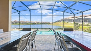 Uma área de refeições coberta ao ar livre, com vista para um lago e casas ao fundo.