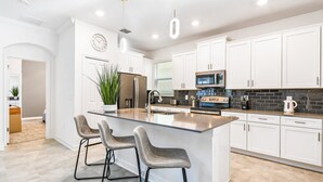 Une cuisine moderne avec des meubles blancs, des appareils en acier inoxydable et un îlot central doté de tabourets de bar.