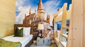 Une chambre à coucher avec une fresque murale sur le thème d’un château, un lit avec des oreillers, une lampe de chevet et un coffre.