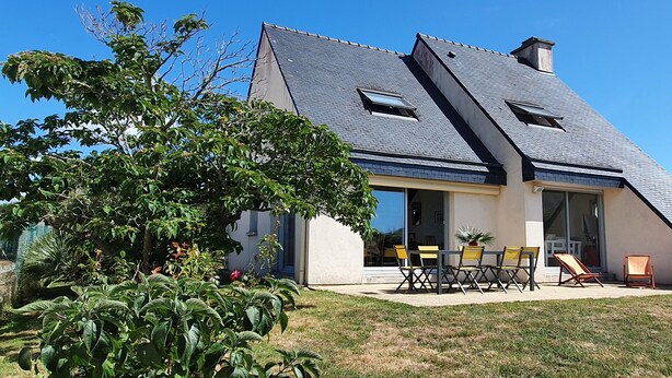 Een modern huis met een schuin dak, grote ramen en een terras met tuinmeubilair.