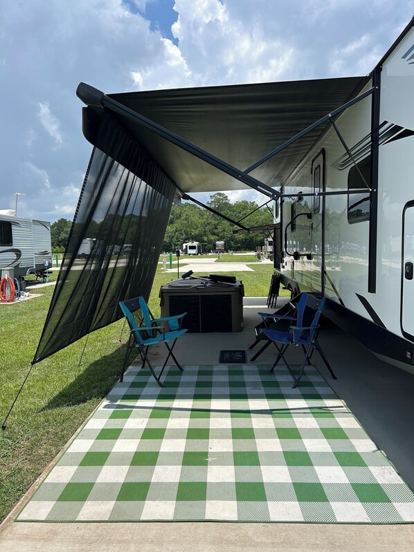A covered outdoor area with a checkered mat, two blue chairs, and a table.