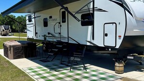 Ein weißer Wohnmobil mit überdachter Terrasse, Grill und kariertem Teppich.