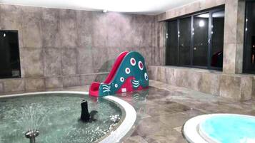 A swimming pool area with a water fountain, a slide, and a jacuzzi.
