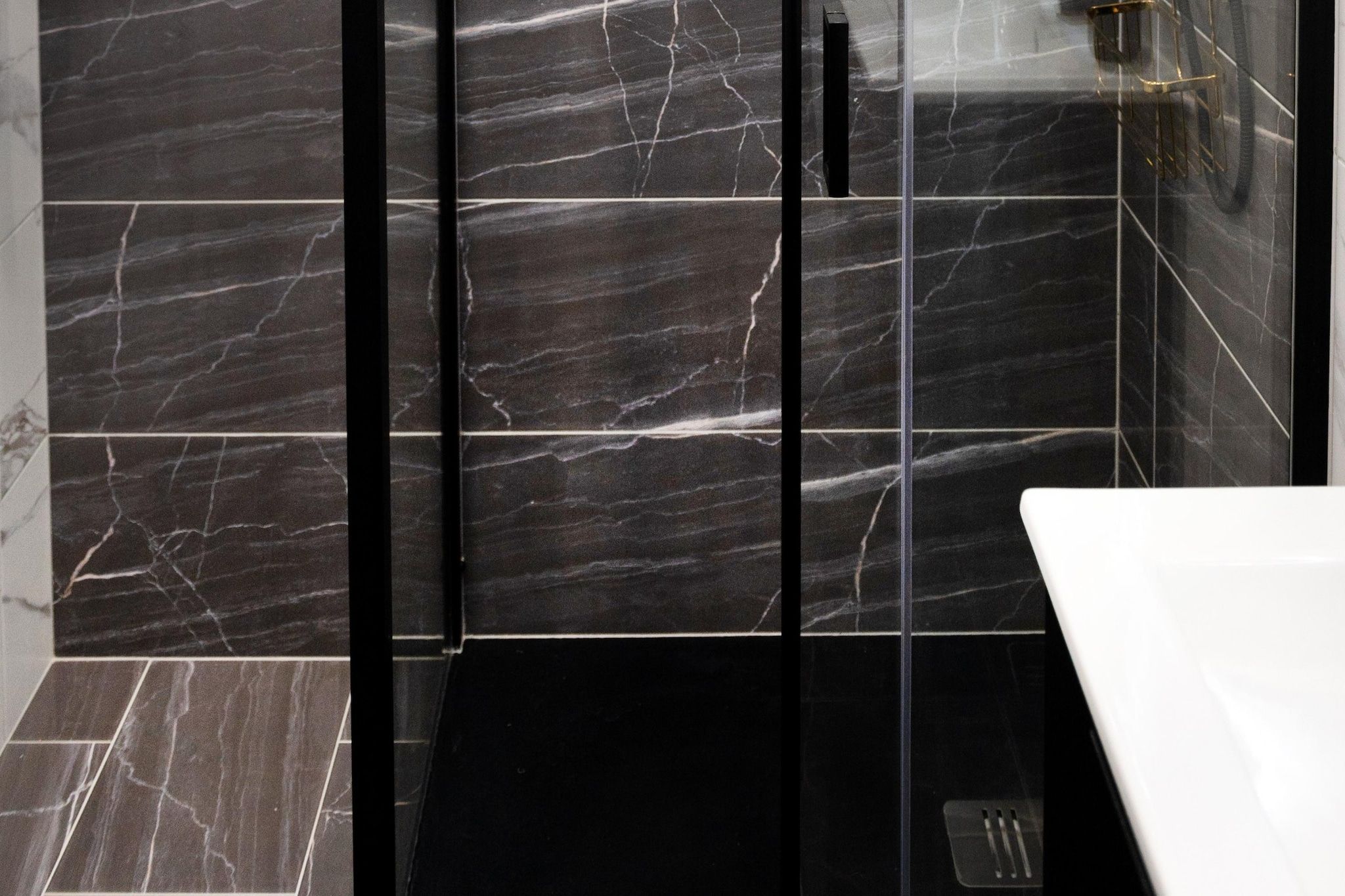 A bathroom with dark marble tiles, a glass shower enclosure, and a white sink.