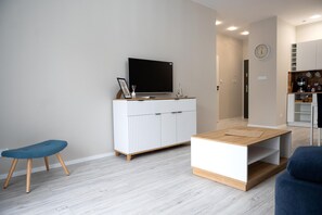 Una sala moderna con un televisor de pantalla plana sobre un mueble blanco, un banco azul y una mesa de centro de madera.