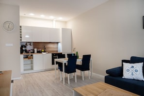 A modern kitchen with white cabinets, a dining table with chairs, and a dark blue sofa with a decorative pillow.