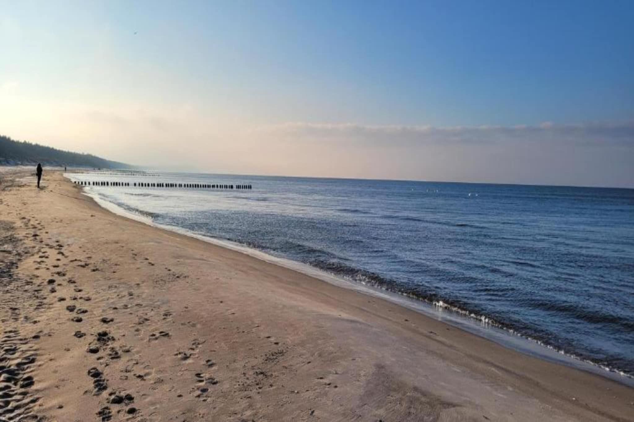 A beach with a wooden pier extending into the water, sandy shore, and footprints.