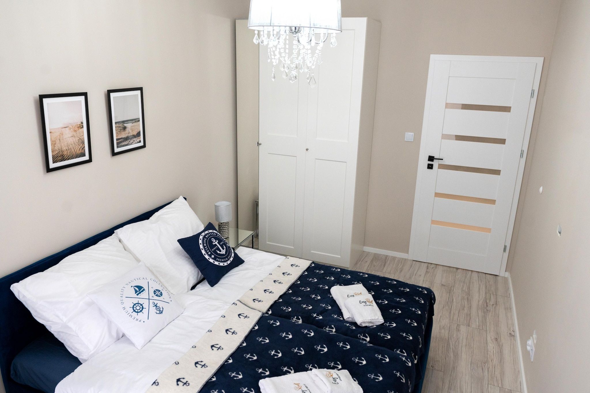 A bedroom with a bed, a chandelier, a door, and two framed pictures on the wall.