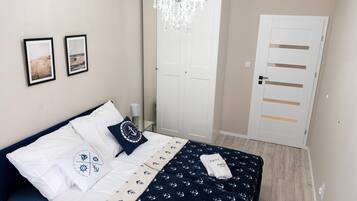 A bedroom with a bed, a chandelier, a door, and two framed pictures on the wall.