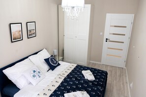 Un dormitorio con cama, candelabro, una puerta y dos cuadros en la pared.