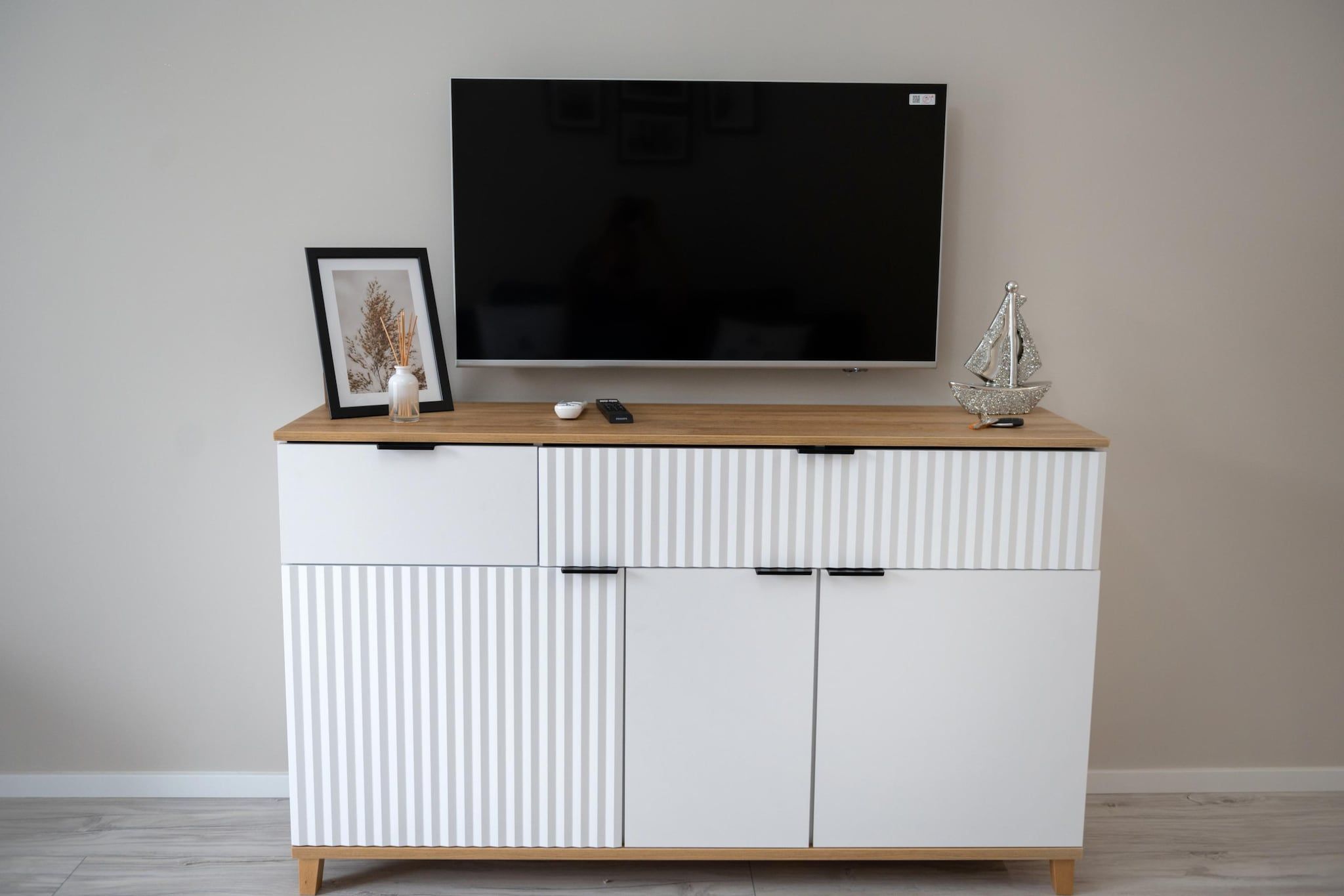 A white TV stand with a flat-screen TV mounted above it, a framed picture, and a small decorative item on top.