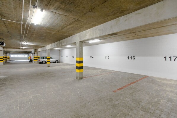 Un estacionamiento con pilares de hormigón, espacios de estacionamiento numerados y una pared blanca con números negros.