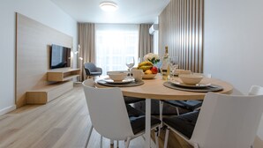A modern dining area with a round wooden table, white chairs, and a television mounted on a wooden panel. - Apartment with river view, sauna, and indoor pool (Dziwnow)