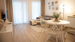 Ein modernes Wohnzimmer mit einer Couch, einem Esstisch mit Stühlen und einem großen Fenster mit Vorhängen.