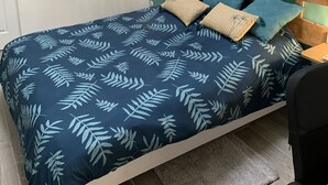 Un dormitorio ordenado con una cama, una mesita de noche, una lámpara, un cuadro enmarcado y vistas al exterior.