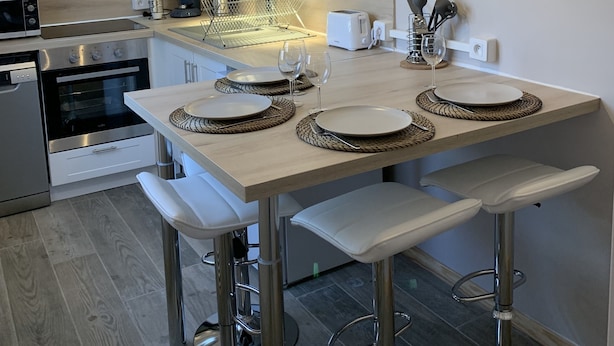 Una cocina moderna con armarios blancos, horno de acero inoxidable, lámpara colgante y un reloj de pared.