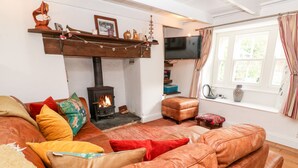 A cozy living room with a fireplace, leather sofas, and a television. - Honeysuckle Cottage (St. Agnes)