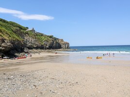 Una playa con acantilados rocosos, cielo despejado y kayaks en la arena.