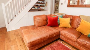 A brown leather sofa with colorful cushions, a wooden staircase, and a red rug. - Honeysuckle Cottage (St. Agnes)
