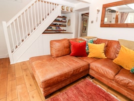 A brown leather sofa with colorful cushions, a wooden staircase, and a red rug.