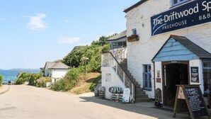 A coastal building named "The Driftwood Sp" with a signboard advertising a B&B and BBQ. - Honeysuckle Cottage (St. Agnes)