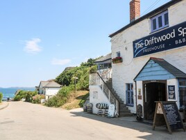 Un edificio costero con un letrero que dice 'The Driftwood Sp. FREEHOUSE B&B' y un cartel para 'Lower Deck' con la descripción de perros bien educados.
