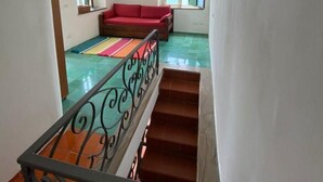 Eine Treppe führt zu einem Wohnbereich mit einem roten Sofa, einem farbenfrohen Teppich und Meerblick durch ein Fenster.