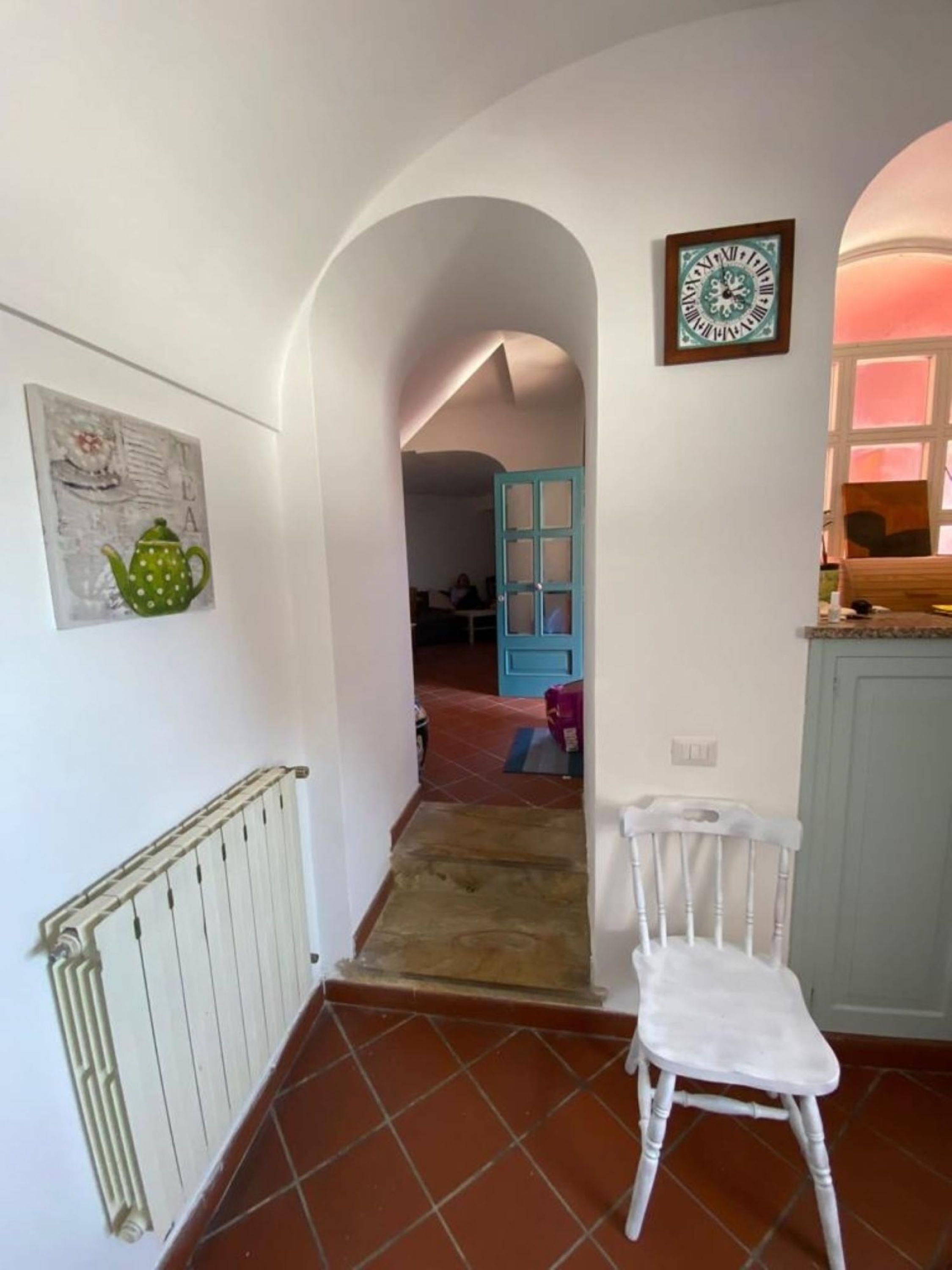 A hallway with a radiator, a white chair, a green teapot artwork, and a clock on the wall.