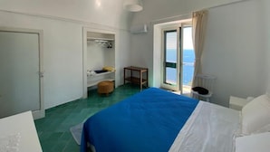 Ein Schlafzimmer mit Bett, Kleiderschrank, einem kleinen Tisch und Meerblick durch ein Fenster.