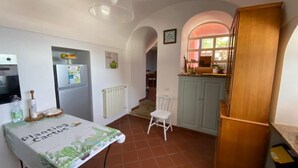 Eine kleine Küche mit einem Tisch, der mit einem 'Planting Cactus'-Tuch bedeckt ist, einem Kühlschrank, einem weißen Stuhl und einem Holzschrank.