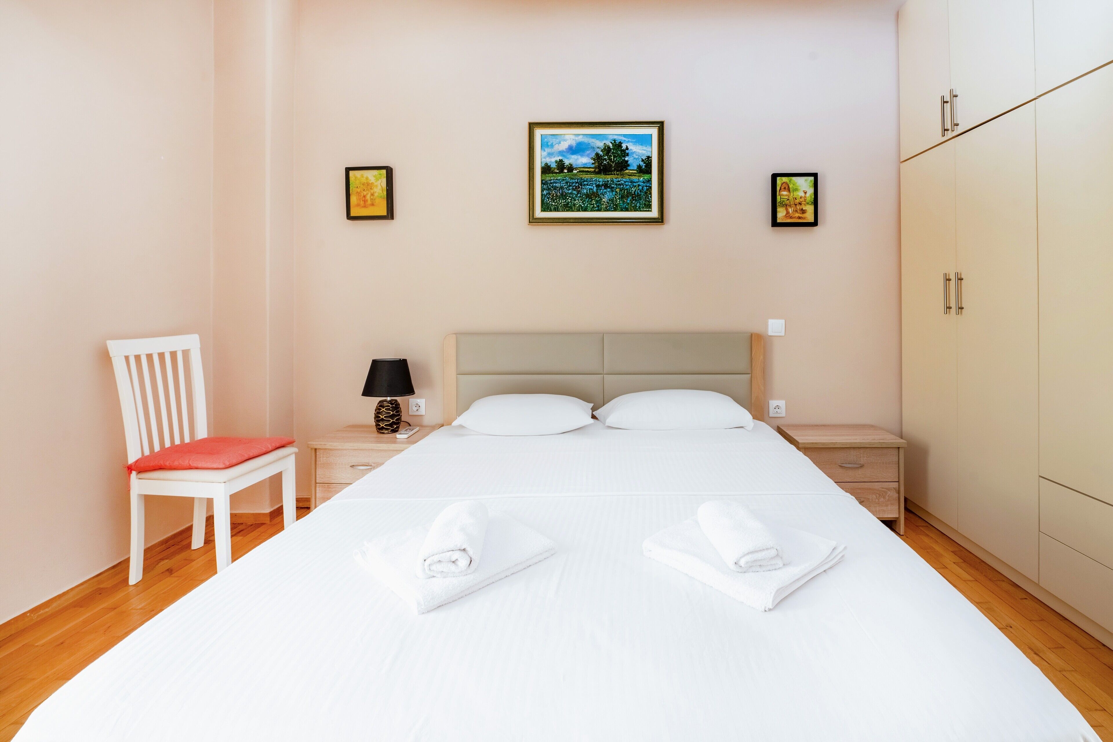 A neatly arranged hotel room with a large bed, a chair, a nightstand, and a wardrobe.