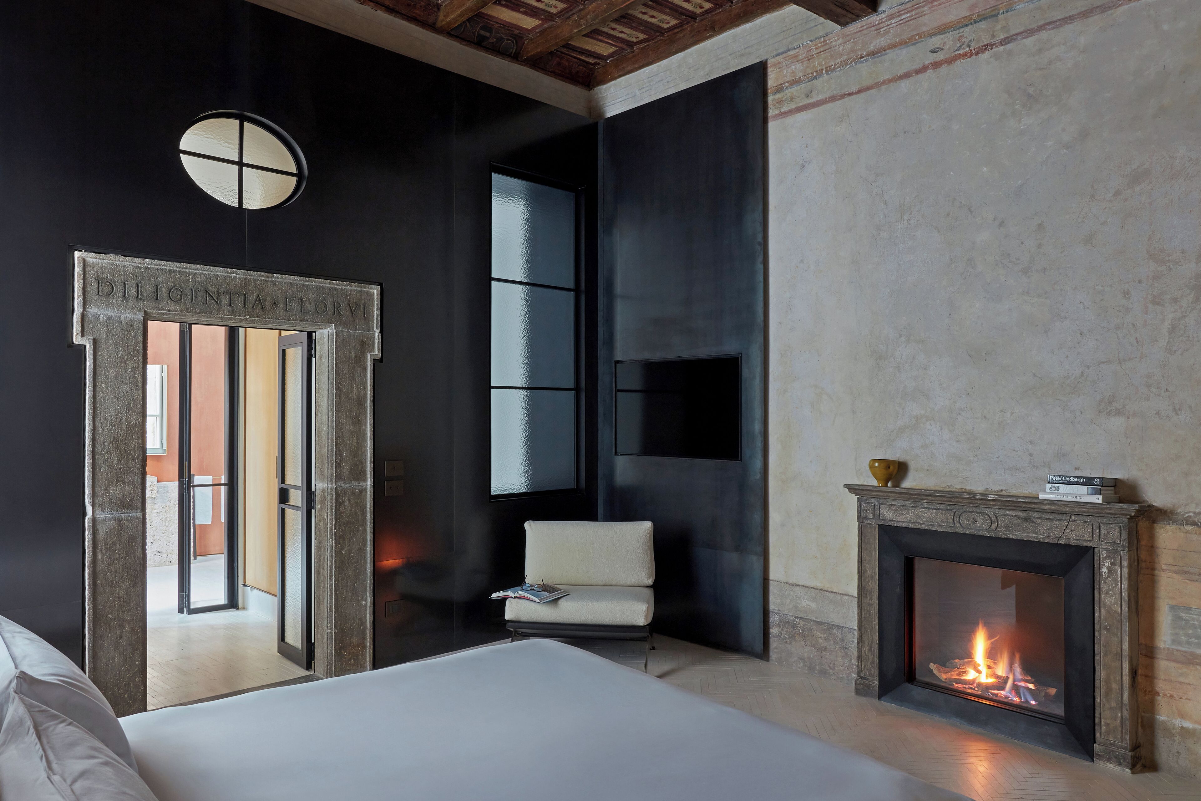 A modern hotel room with a fireplace, a large window, and a door labeled "DILIGENTIA FLORM".