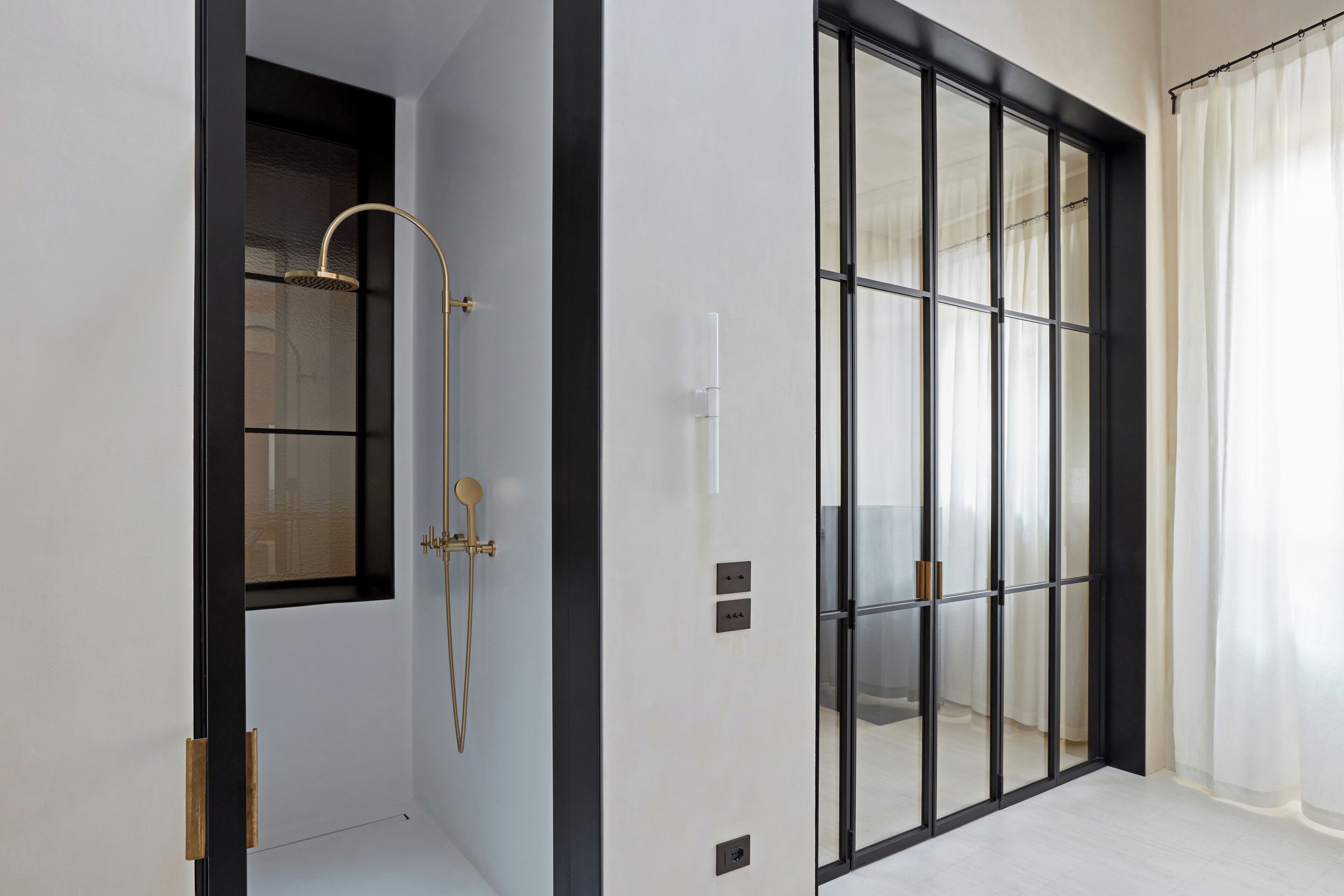 Un baño moderno con cabina de ducha de vidrio, inodoro empotrado y un amplio ventanal con cortinas.