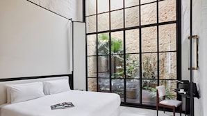 Camera d'albergo moderna con un letto grande, una sedia e vista su un cortile con piante.