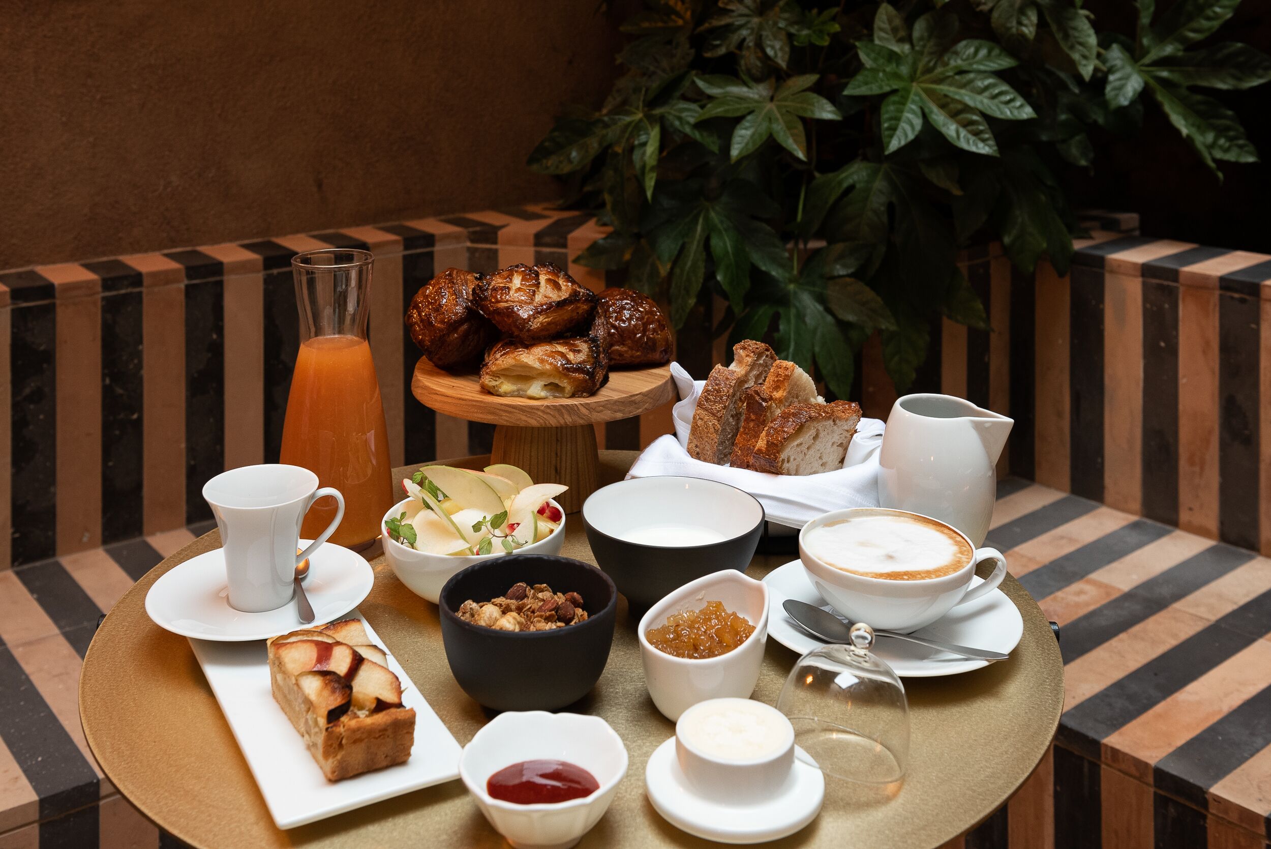 Una mesa dispuesta con diversas opciones para el desayuno, incluyendo pasteles, un frutero y bebidas.