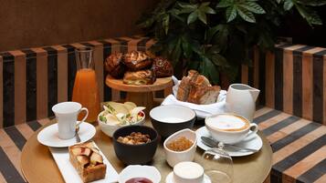 Una mesa dispuesta con diversas opciones para el desayuno, incluyendo pasteles, un frutero y bebidas.
