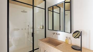 A bathroom with a glass-enclosed shower, a beige sink with a black countertop, and a mirror with a round frame.